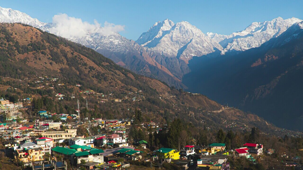 small town in munsiyari with snow covered mountains in the background