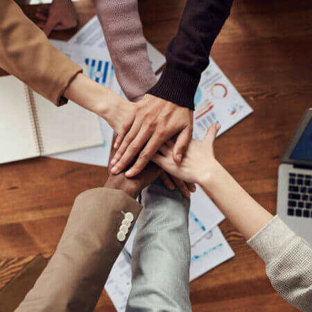 people stacking hands in workplace displaying teamwork